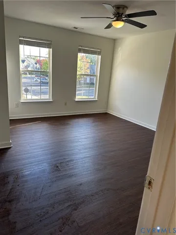 an empty room with wooden floor fan and windows