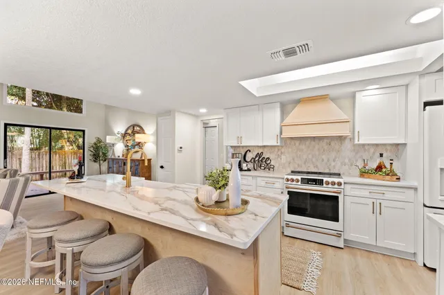 a kitchen with granite countertop a stove a sink and white cabinets with wooden floors