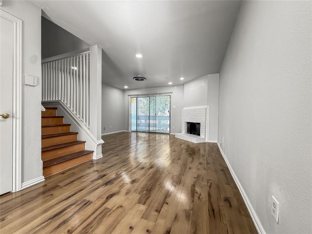 5840 Spring Valley Road, Unit 1104 Dallas, TX 75254 - Photo 8 of 16 Spacious living area featuring wood-finish flooring, a white-painted brick fireplace, and sliding glass doors
