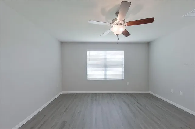 an empty room with wooden floor chandelier fan and windows