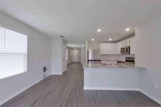 a living room with stainless steel appliances wooden floors and kitchen view