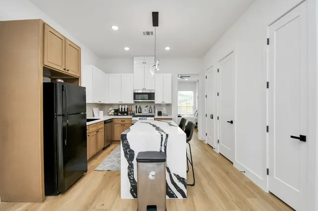 a kitchen with stainless steel appliances granite countertop a refrigerator a oven a sink a dining table and chairs with wooden floor