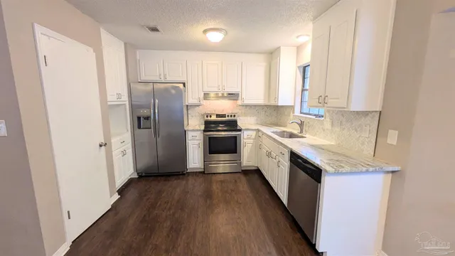 a kitchen with stainless steel appliances granite countertop a stove top oven a refrigerator a sink and dishwasher with wooden floor