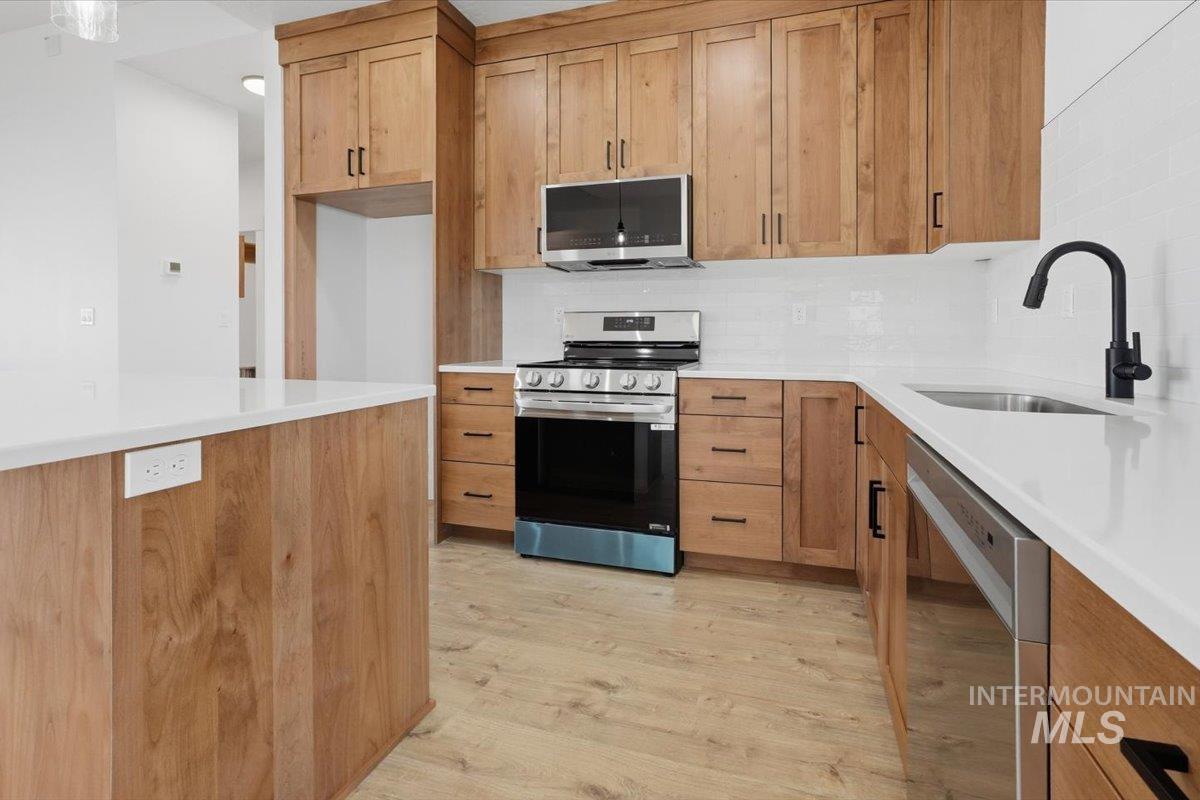 2173 Austin Way Fruitland, ID 83619 - Photo 8 of 28 Kitchen featuring stainless steel appliances, wood finish cabinetry, light wood-type flooring, and backsplash