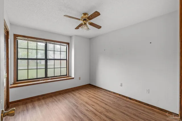 an empty room with wooden floor fan and windows