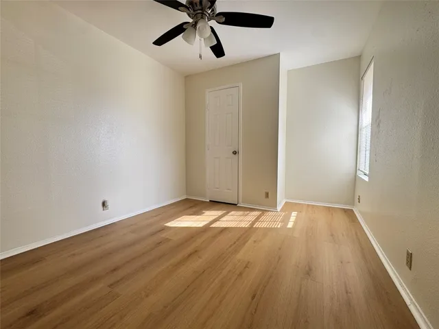 an empty room with wooden floor fan and windows