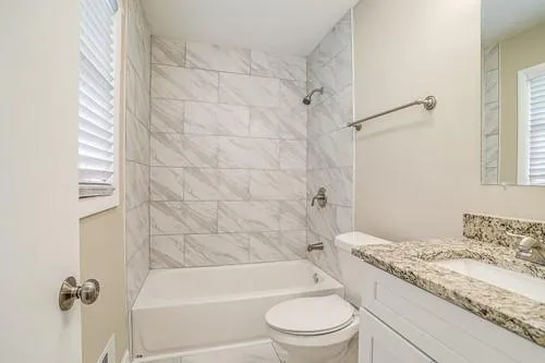 a bathroom with a granite countertop bathtub shower sink vanity and toilet