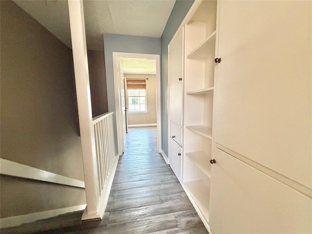 8001 Rothington Road, Unit 33 Dallas, TX 75227 - Photo 10 of 15 Hallway featuring wood-finish flooring, built-in cabinetry with open shelving and closed storage, and a white balustrade
