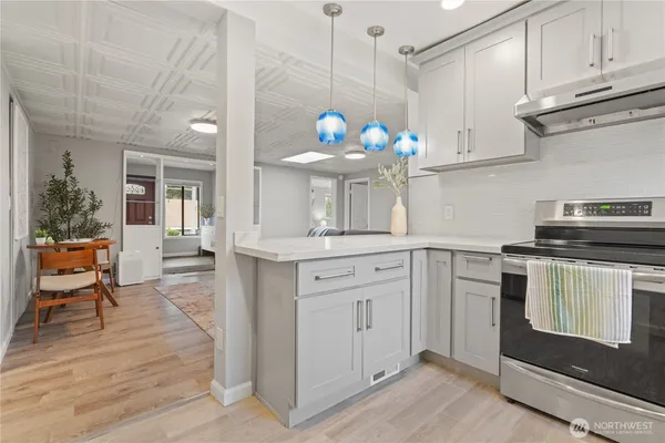 a kitchen with stainless steel appliances granite countertop a stove a sink dishwasher and white cabinets with wooden floor