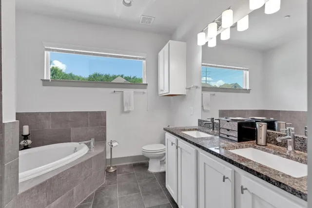 a bathroom with a granite countertop sink a toilet a bathtub and a window