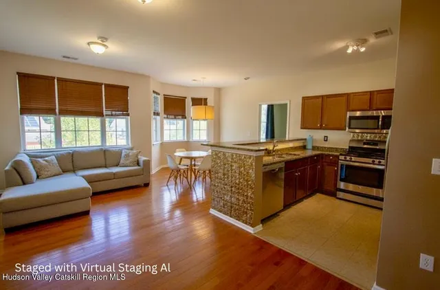 a living room with stainless steel appliances granite countertop a couch a stove a kitchen island with large windows and wooden floor