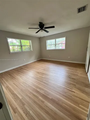 an empty room with wooden floor ceiling fan and windows