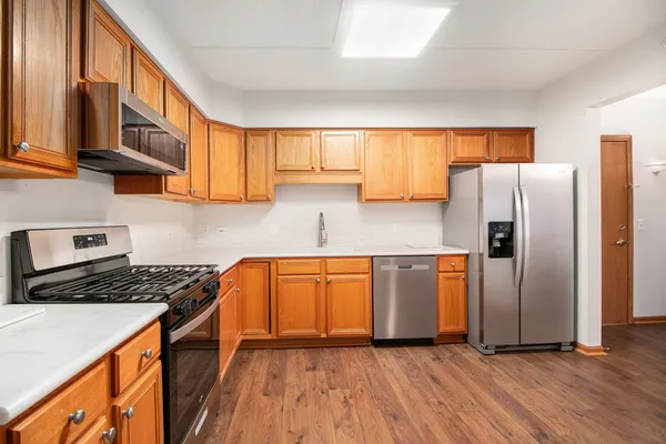 a kitchen with stainless steel appliances granite countertop a refrigerator a sink dishwasher a stove with wooden cabinets and floor