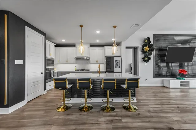 a kitchen with stainless steel appliances kitchen island granite countertop dining table chairs and a wooden floor