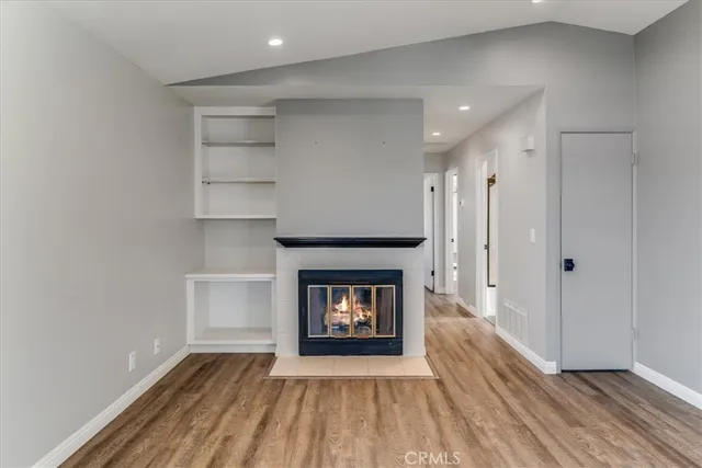 a view of an empty room with wooden floor fireplace and a window