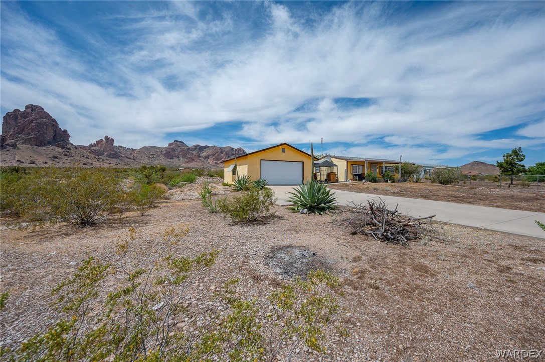 2465 Egar Road Golden Valley, AZ 86413 - Photo 79 of 98 Property with a concrete driveway leading to a garage with a white door, set against a backdrop of desert landscape and rock formations