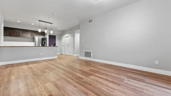 an empty room with wooden floor and kitchen view
