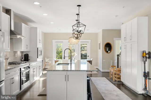 a kitchen with stainless steel appliances kitchen island granite countertop a stove a sink a refrigerator and white cabinets with wooden floor