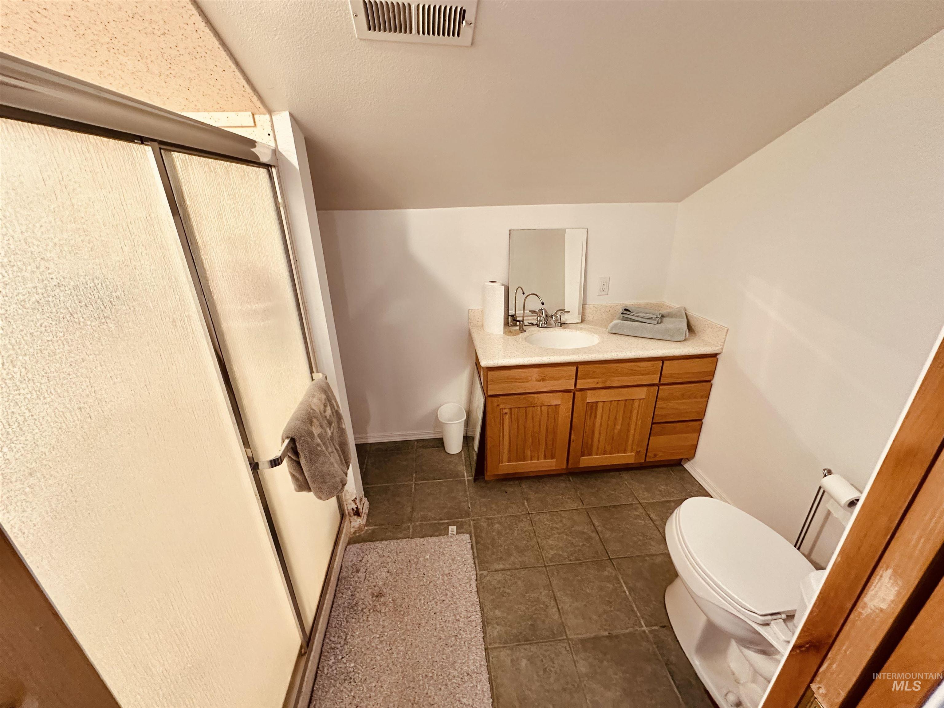 1049 Grand Avenue Nyssa, OR 97913 - Photo 22 of 50 Bathroom featuring a vanity with a light-toned countertop and wood-finish cabinetry, a white toilet, and a shower with textured glass doors