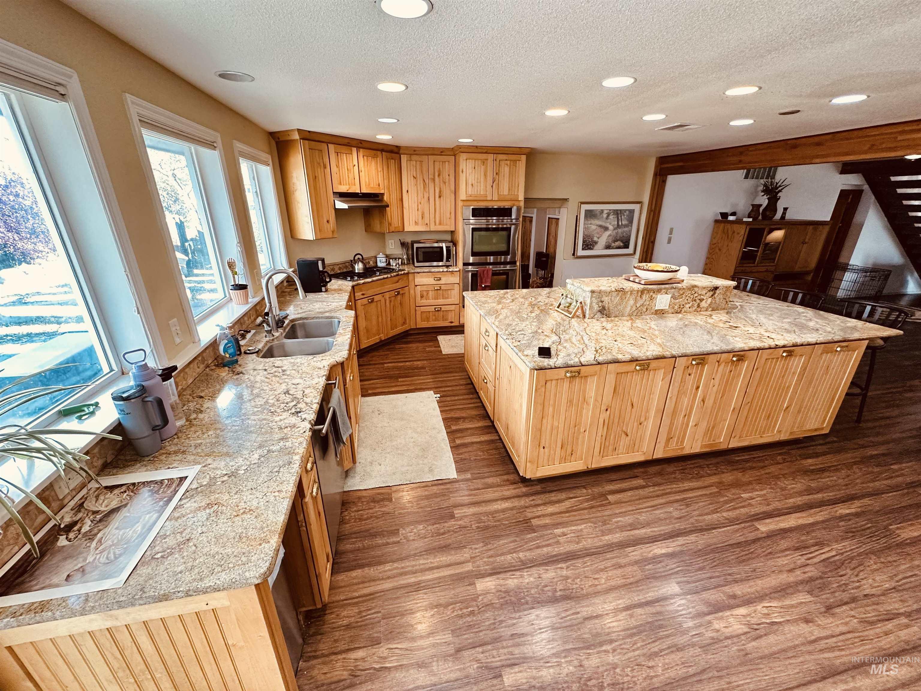 1049 Grand Avenue Nyssa, OR 97913 - Photo 6 of 50 Spacious kitchen featuring a large central island with a tiered countertop, extensive perimeter countertops, wood-finish flooring, recessed lighting, and multiple windows