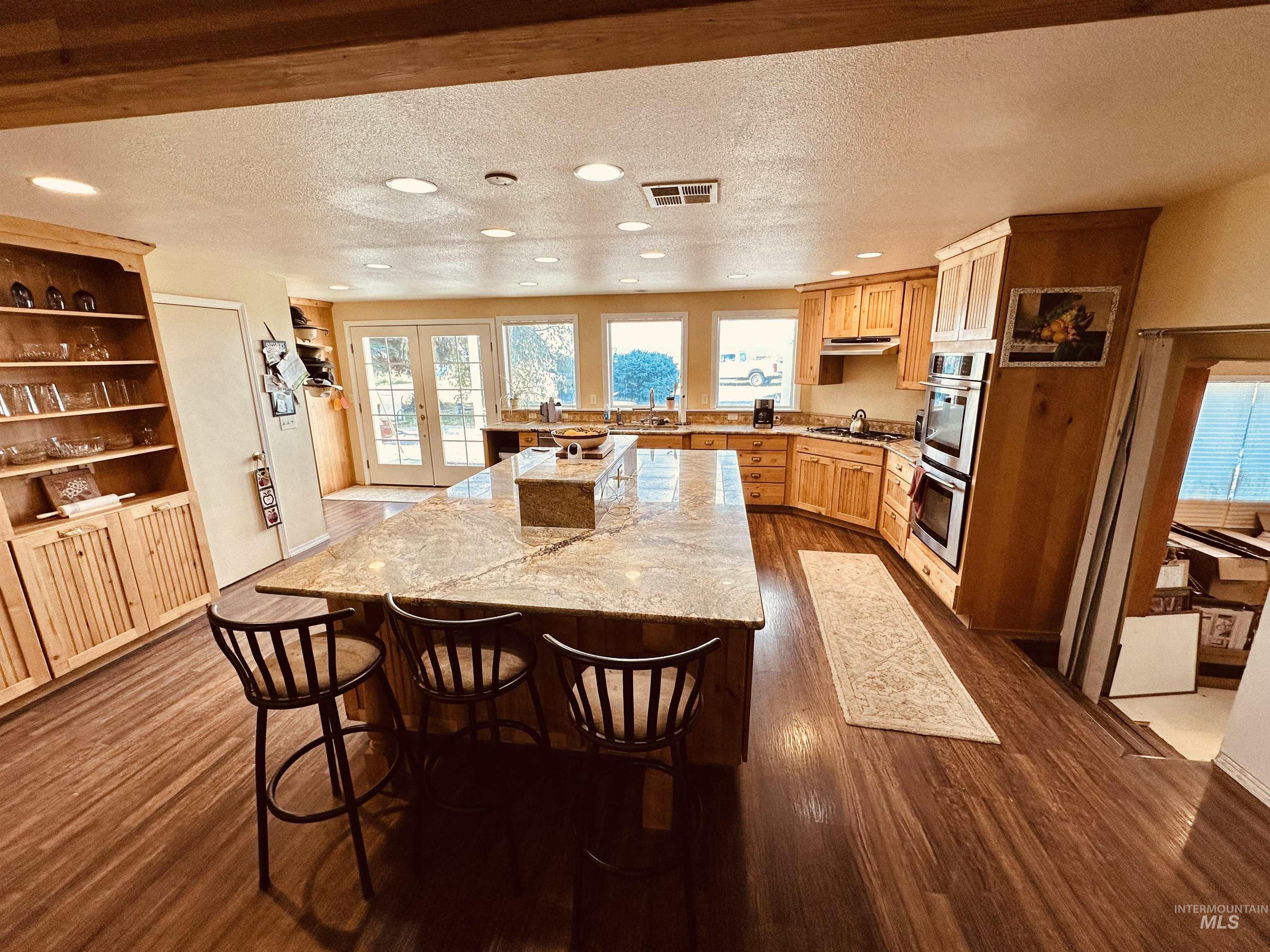 1049 Grand Avenue Nyssa, OR 97913 - Photo 9 of 50 Spacious kitchen featuring a large island with a stone-finish countertop, wood-finish flooring, abundant wooden cabinetry, stainless steel double ovens, and multiple windows with patio access