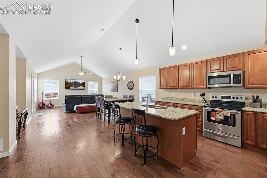 6565 Watusi Road Peyton, CO 80831 - Photo 9 of 36 a open kitchen with stainless steel appliances granite countertop a stove a refrigerator a kitchen island a dining table and chairs with wooden floor