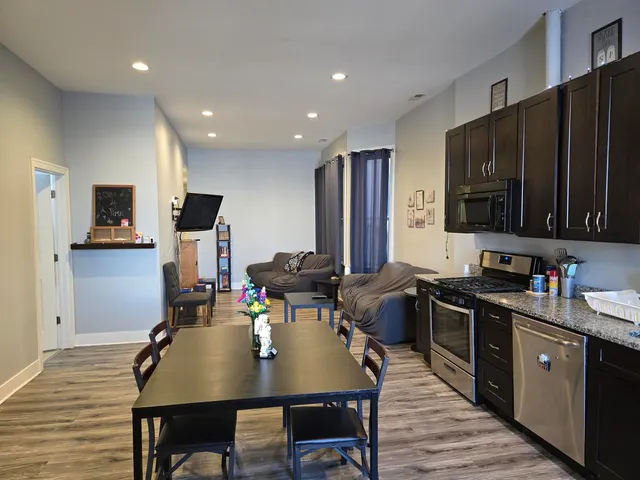 a open kitchen with stainless steel appliances granite countertop a stove top oven a sink dishwasher a dining table and chairs with wooden floor