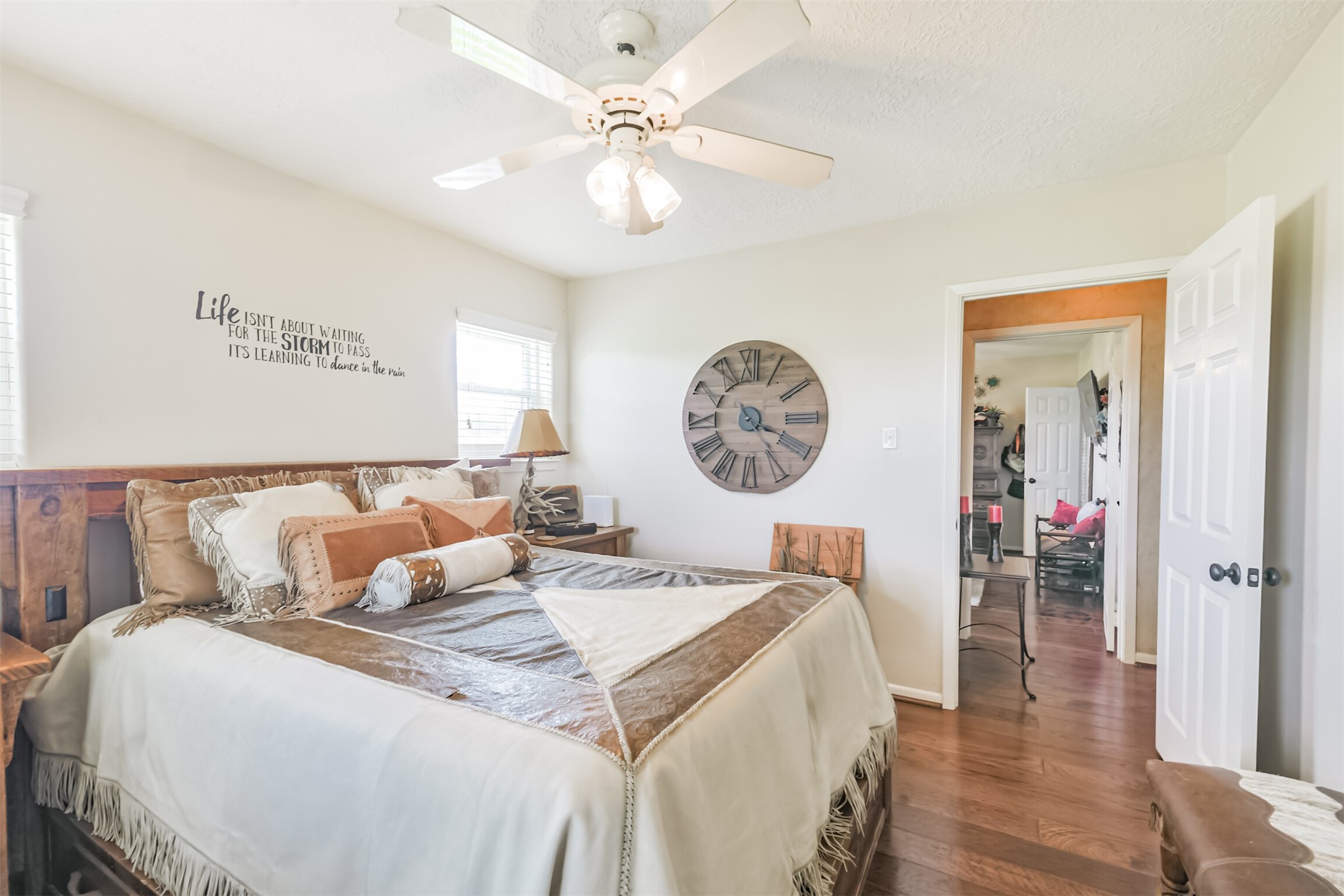 307 West Hufsmith Road Tomball, TX 77375 - Photo 26 of 44 Cozy bedroom featuring warm hardwood floors, a ceiling fan, and rustic decor with a large clock accent.