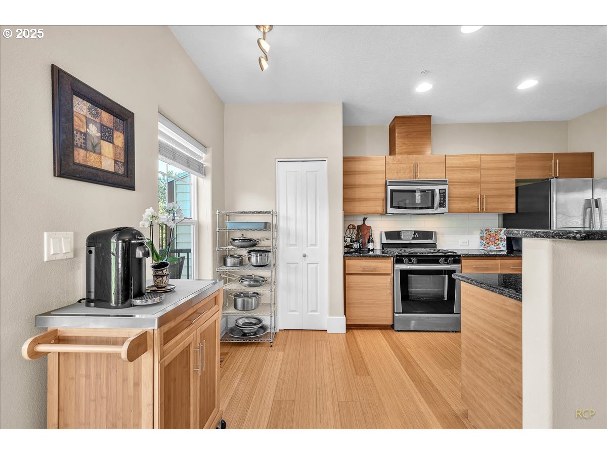 794 Northwest 118th Avenue, Unit 101 Portland, OR 97229 - Photo 14 of 41 a kitchen with stainless steel appliances kitchen island granite countertop a refrigerator oven a sink dishwasher and wooden cabinets with wooden floor