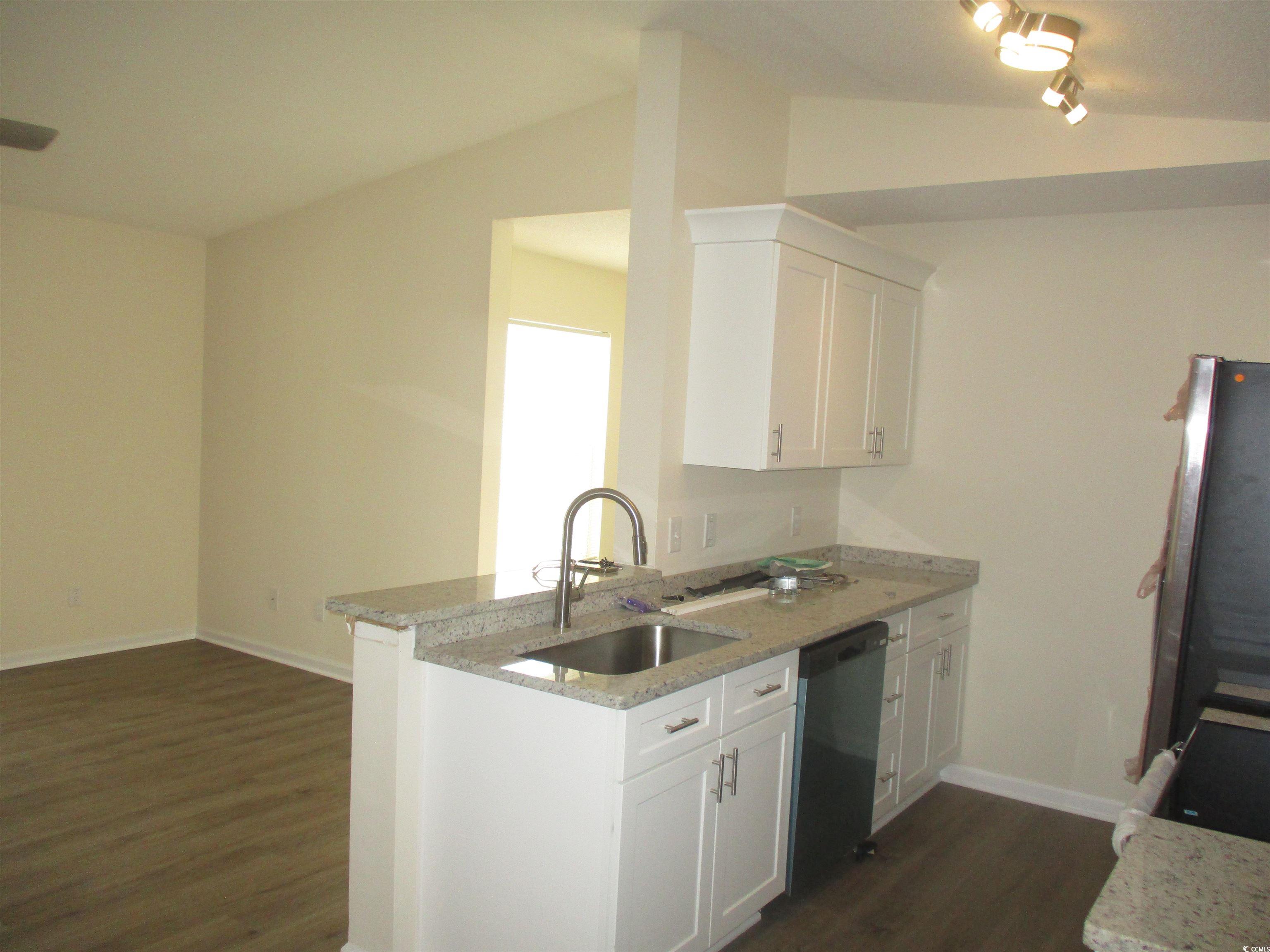 8545 Hopkins Circle Surfside Beach, SC 29575 - Photo 10 of 24 Kitchen featuring light stone countertops, white cabinetry, dark wood-style flooring, stainless steel dishwasher, and lofted ceiling