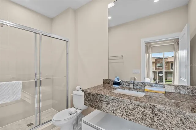 a bathroom with a granite countertop sink a toilet a mirror and shower