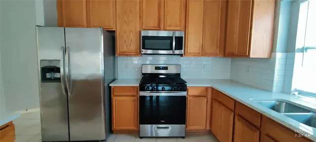 a kitchen with stainless steel appliances granite countertop a refrigerator a stove and a sink with wooden cabinets