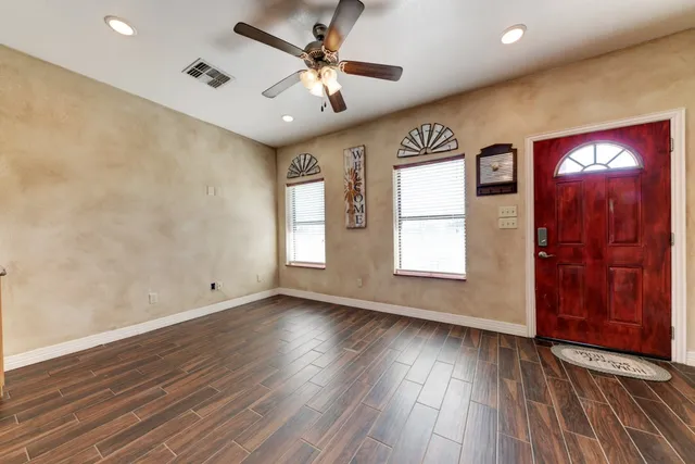 a view of an empty room with wooden floor and a ceiling fan