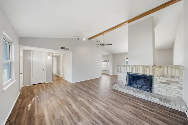 a view of an empty room with wooden floor fireplace and a window