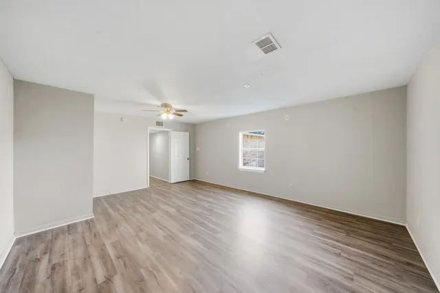 an empty room with wooden floor ceiling fan and windows