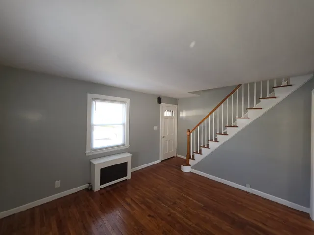 a view of an empty room with wooden floor fireplace and a window