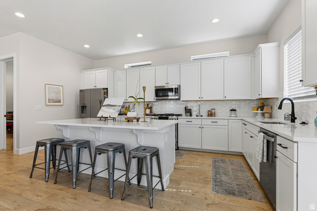 839 Walker Way St. George, UT 84770 - Photo 6 of 32 Open-concept kitchen featuring white shaker cabinetry, an expansive central island with seating, stainless steel appliances, a white tile backsplash, and light wood-finish flooring