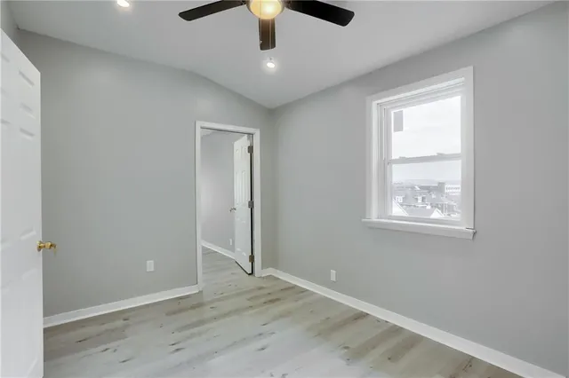 an empty room with wooden floor chandelier fan and windows