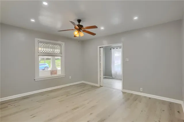 an empty room with wooden floor chandelier fan and windows