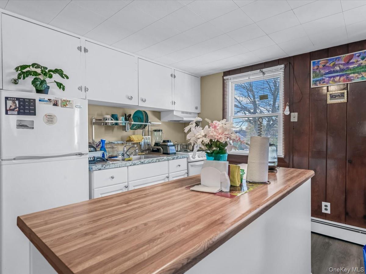 205 Lenox Road Huntington Station, NY 11746 - Photo 15 of 25 Kitchen featuring white cabinetry, white appliances, under cabinet range hood, a baseboard radiator, and butcher block countertops