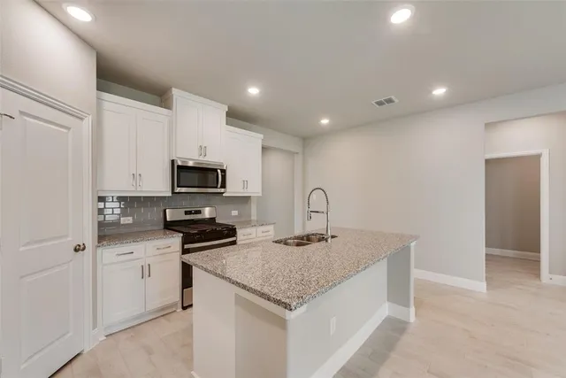 a kitchen with granite countertop a sink stainless steel appliances and white cabinets