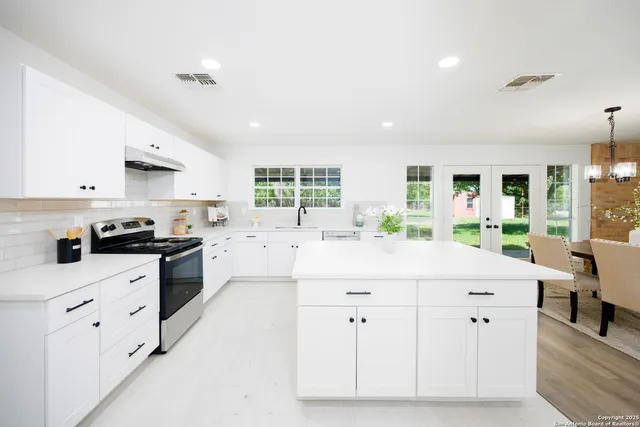 a kitchen with stainless steel appliances kitchen island granite countertop a stove a sink a refrigerator white cabinets and couches with wooden floor