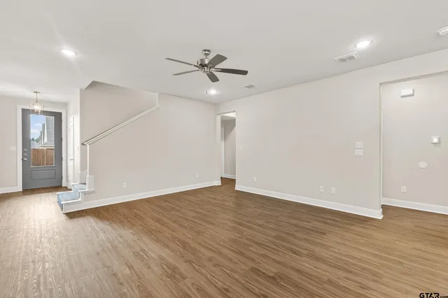 an empty room with wooden floor ceiling fan and windows