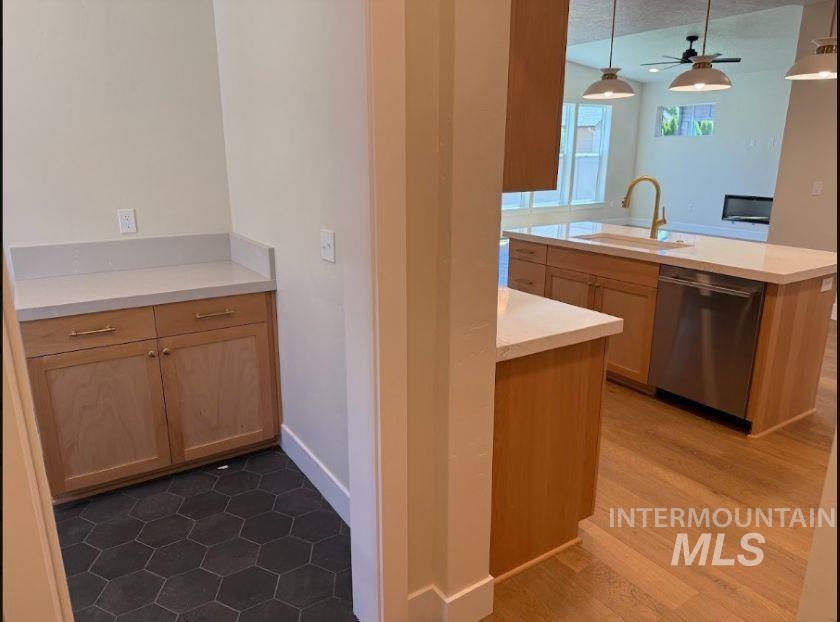 683 West Wrangler Street Meridian, ID 83646 - Photo 8 of 23 Open-concept kitchen featuring light wood cabinetry, white countertops, a central island with an undermount sink and gold-finish faucet, a stainless steel dishwasher, and wood-finish flooring