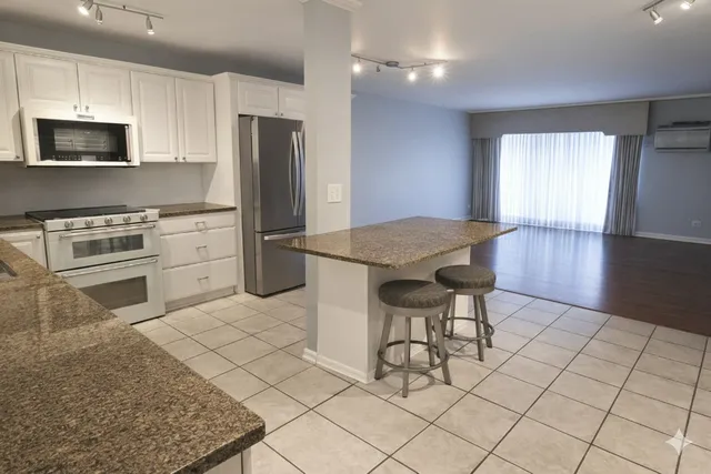 a kitchen with stainless steel appliances granite countertop a stove a sink dishwasher a refrigerator and a microwave with wooden floor