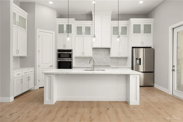 a kitchen with stainless steel appliances granite countertop a sink a microwave a refrigerator and white cabinets with wooden floor