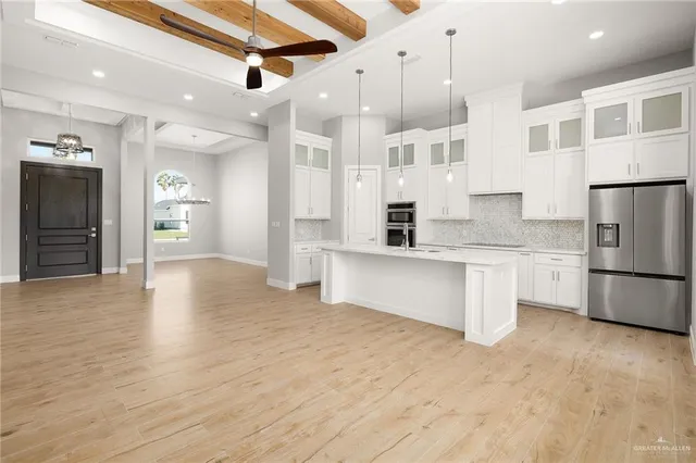 a large kitchen with stainless steel appliances granite countertop a refrigerator a sink dishwasher and white cabinets with wooden floor