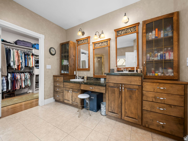 1317 South Pond Circle Mapleton, UT 84664 - Photo 14 of 63 Primary bathroom featuring twin wood vanities with undermount sinks and dark countertops, individual mirrors, built-in cabinetry with glass doors, and light tile flooring