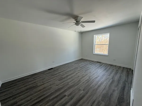 an empty room with wooden floor fan and windows