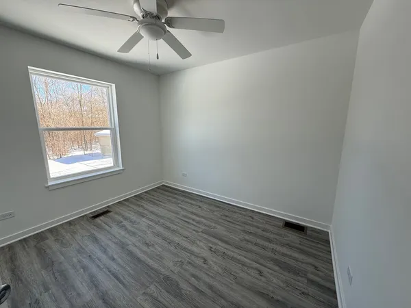 an empty room with wooden floor chandelier fan and windows